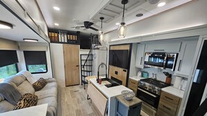 A compact RV interior with a kitchenette, a dining area, and a seating space. - Spacious 2025 Destination RV Sleeps 9 (Lorena)