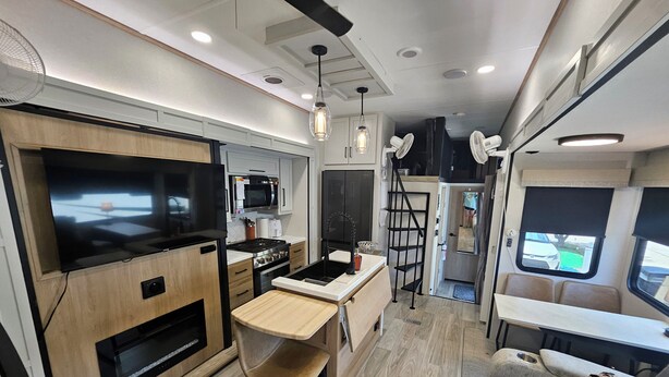 A compact RV kitchen with a stove, microwave, and a dining area with a bench. - Spacious 2025 Destination RV Sleeps 9 (Lorena)