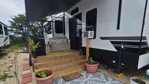 A recreational vehicle with a covered porch, a welcome mat, and potted plants. - Spacious 2025 Destination RV Sleeps 9 (Lorena)