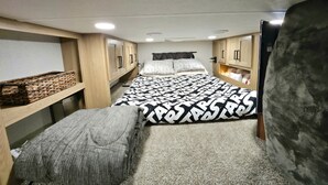 A compact bedroom with a bed, a bench, and built-in wooden cabinets. - Spacious 2025 Destination RV Sleeps 9 (Lorena)