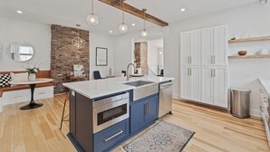 A modern kitchen with a central island, wooden beams, and a brick accent wall. - 3BR Stylish Retreat, Minutes from Downtown Pittsburgh, Free 3-Car Parking (Pittsburgh)