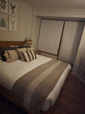 A neatly made bed with a striped blanket and multiple pillows, a bedside lamp, and framed artwork on the wall.