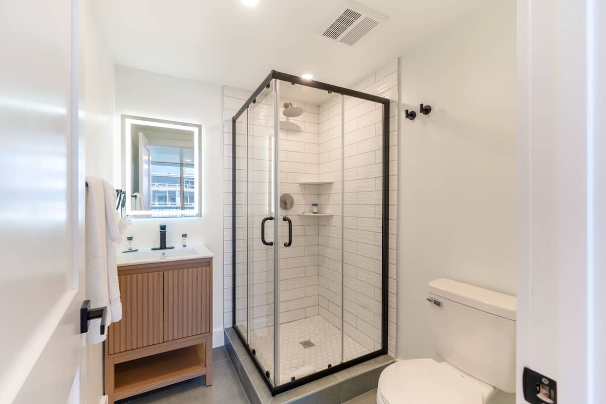 A modern bathroom with a glass-enclosed shower, a wooden vanity, and a white toilet.