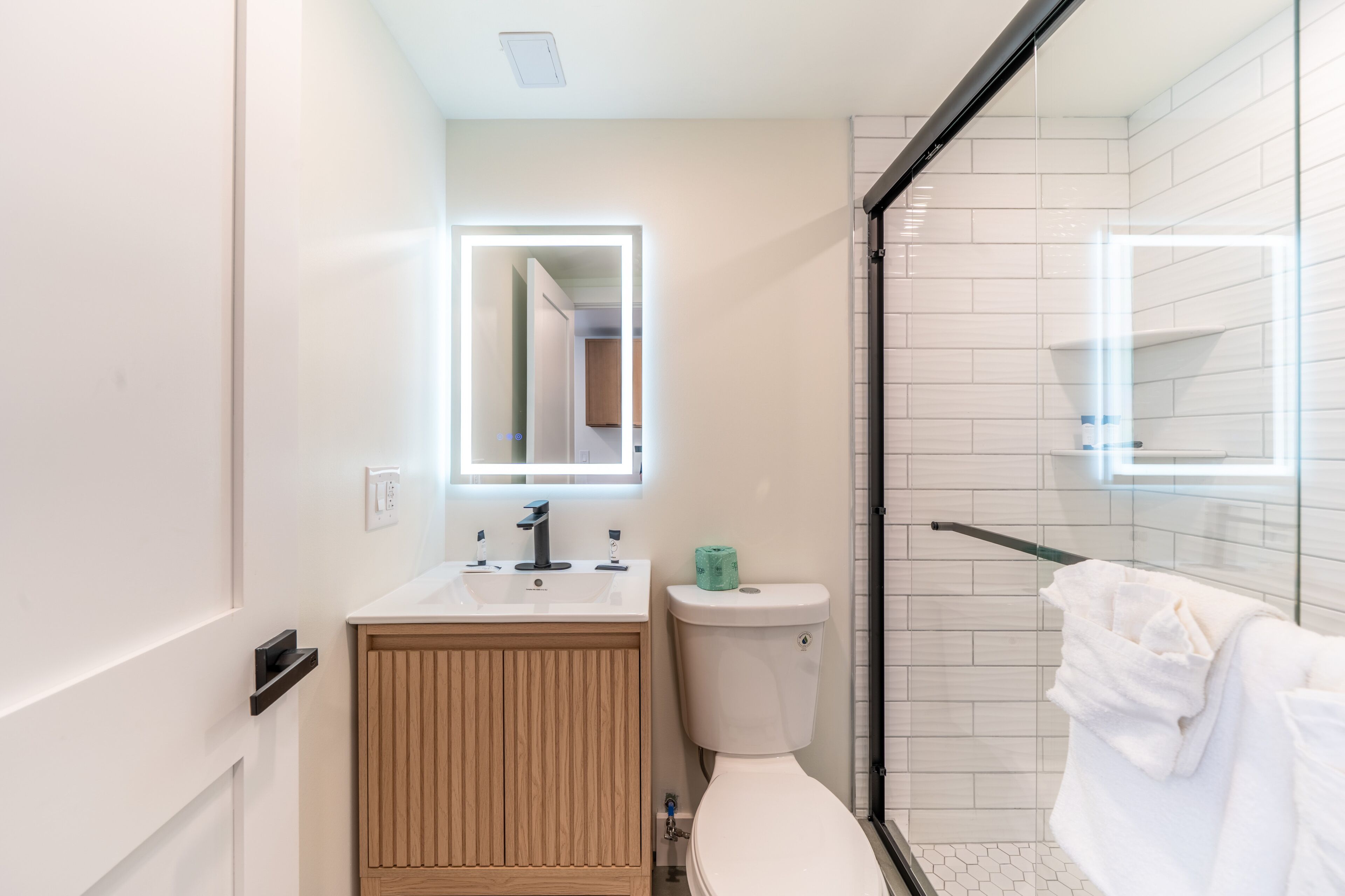 A modern bathroom with a toilet, sink, mirror, and glass shower enclosure.