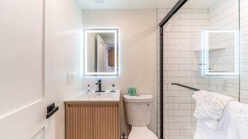 A modern bathroom with a toilet, sink, mirror, and glass shower enclosure.