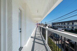 A balcony with a white railing, a view of parked cars, and a building in the background. - Ocean's Edge Luxury Rentals (Ocean City)