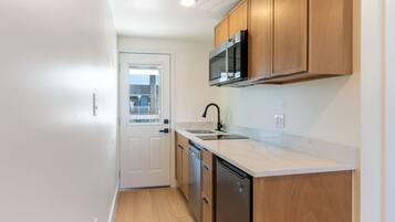 A compact kitchen with wooden cabinets, a microwave, a dishwasher, and a white countertop.