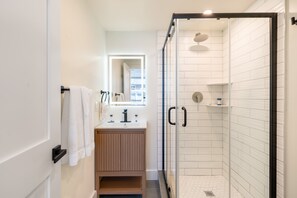 A modern bathroom with a glass-enclosed shower, a wooden vanity, and a mirror with a lighted frame.