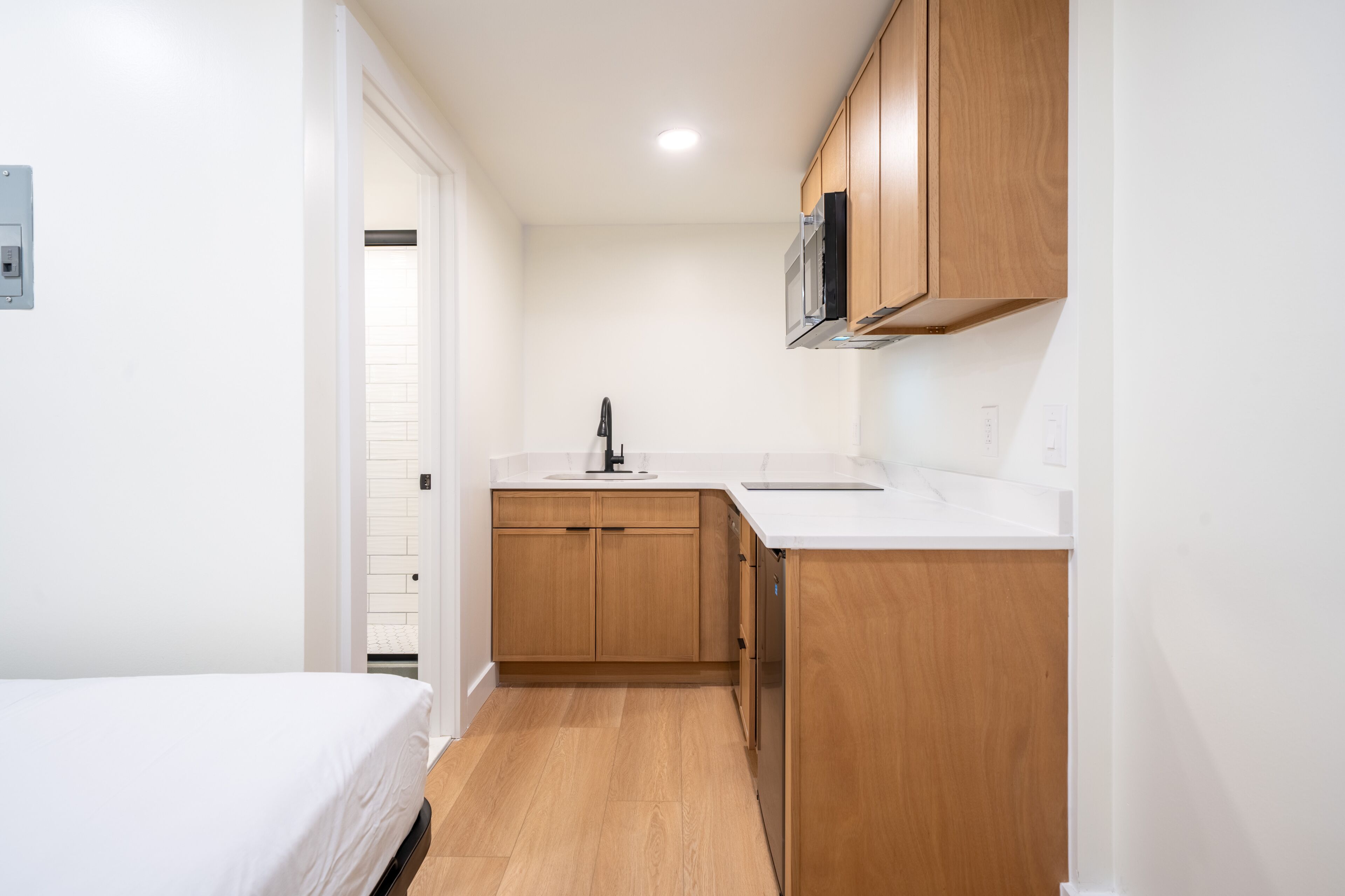 A compact kitchen with wooden cabinets, a white countertop, and a built-in microwave.