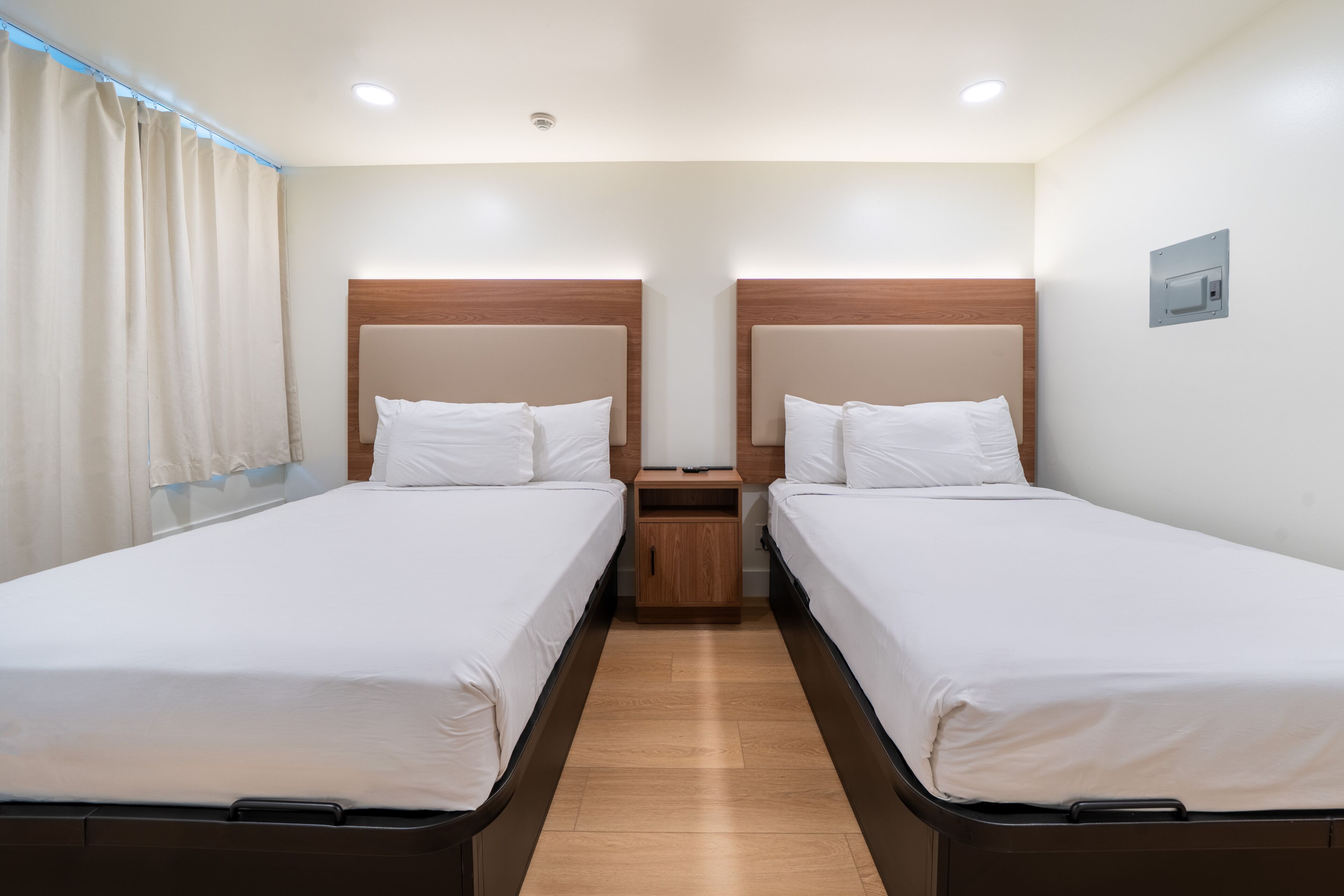 Ein Doppelzimmer mit zwei Betten, Holz-Kopfteilen, einem Nachttisch und einer Deckenleuchte.