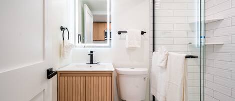 A modern bathroom with a toilet, sink, and glass shower enclosure.