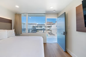A hotel room with a bed, a large window, a balcony, and a door.