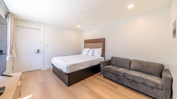 A bedroom with a bed, a gray sofa, and a wooden floor.