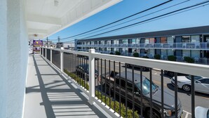 Un hôtel doté d’un balcon donnant sur une rue, avec un panneau indiquant un parking, plusieurs étages et un ciel dégagé.