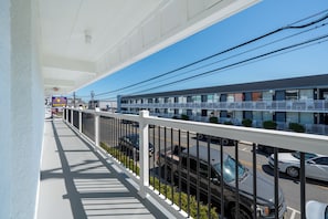 A hotel with a balcony overlooking a street, featuring a parking sign, multiple floors, and a clear sky.