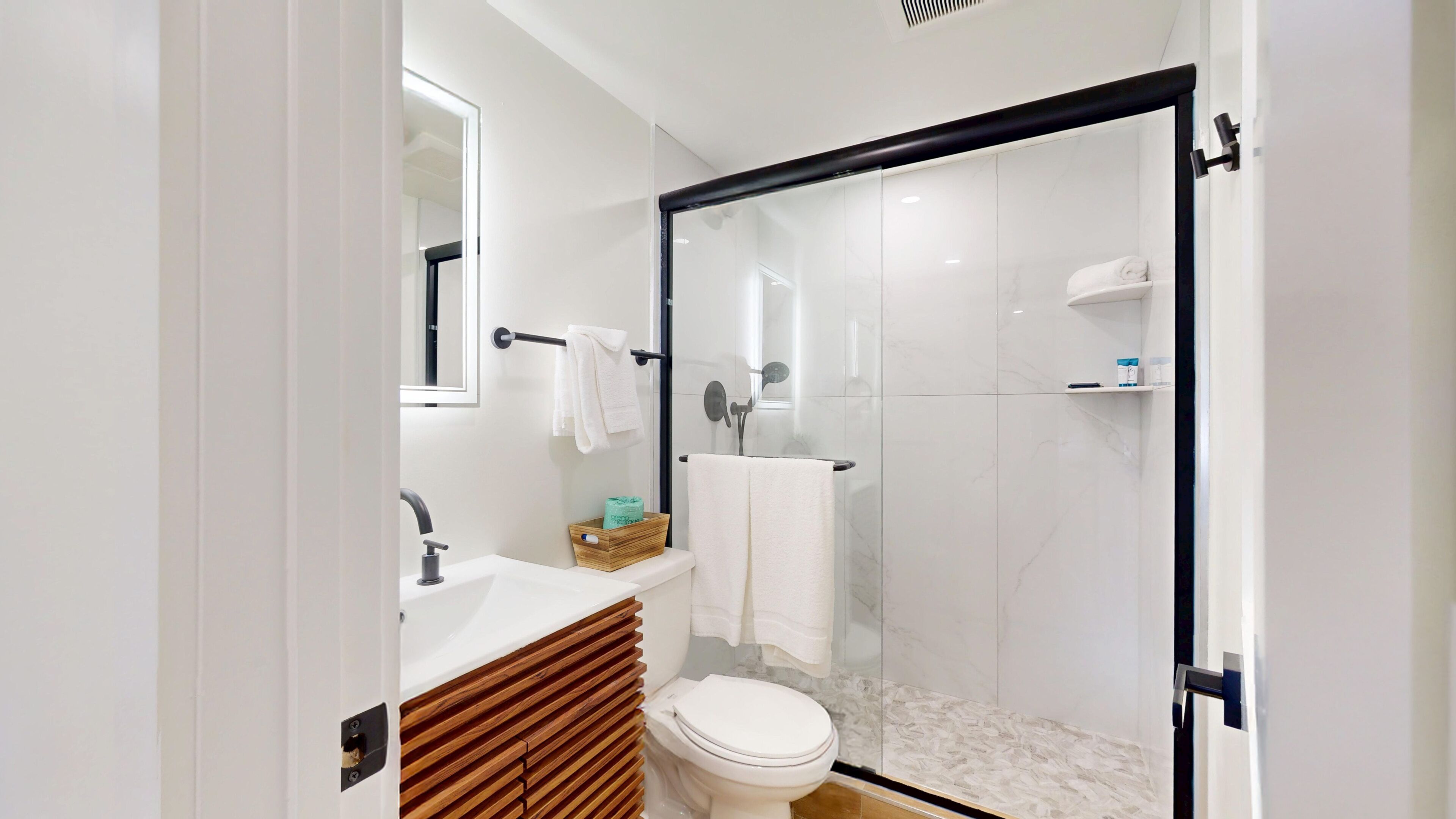 Une salle de bain moderne avec une douche à parois de verre, des toilettes blanches, un meuble-lavabo avec un miroir et un meuble en bois.