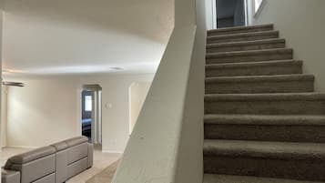 Un escalier menant à un deuxième étage, des marches recouvertes de moquette, un mur de couleur beige et un canapé d’angle dans un salon.