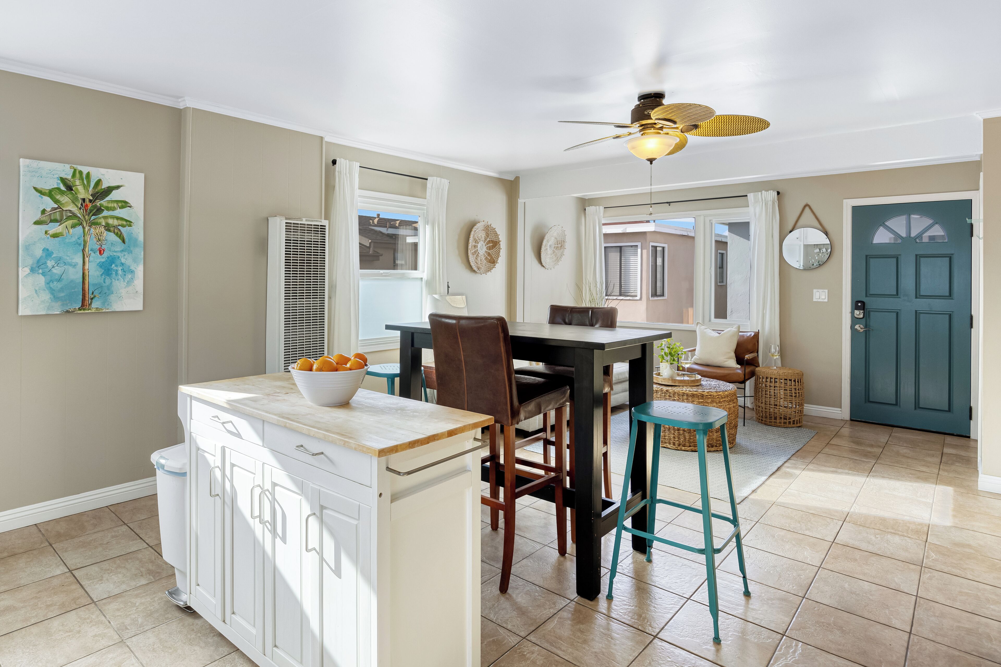 A kitchen with a dining area, white cabinets, a ceiling fan, and a teal door.