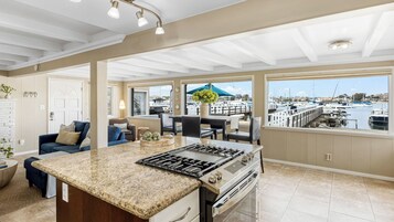 Una cocina amplia con una isla grande, un comedor con vistas al puerto deportivo y una zona de estar acogedora con vistas al muelle.
