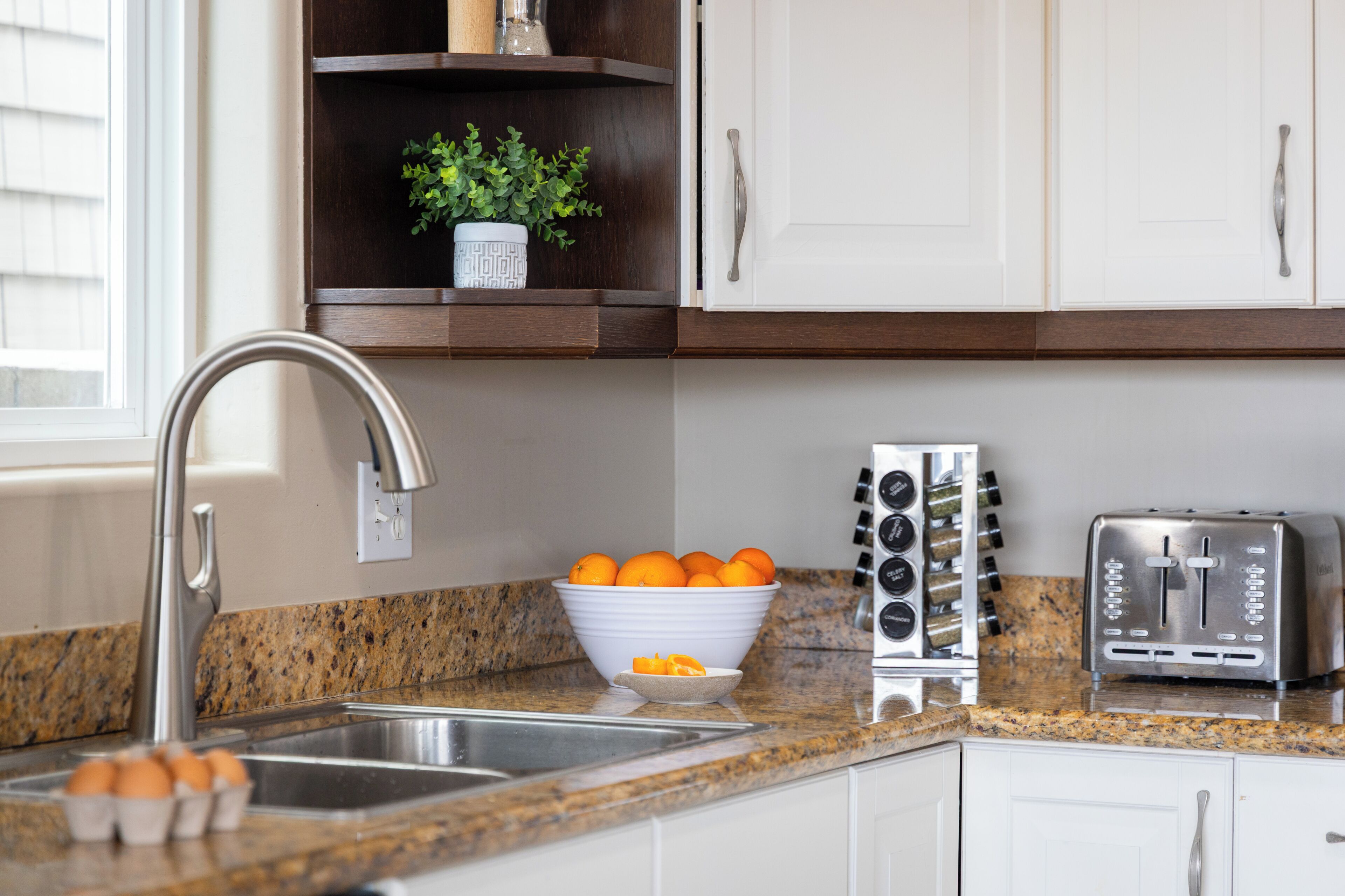 A kitchen with a granite countertop, a sink, a bowl of oranges, a toaster, and a cabinet with a plant.