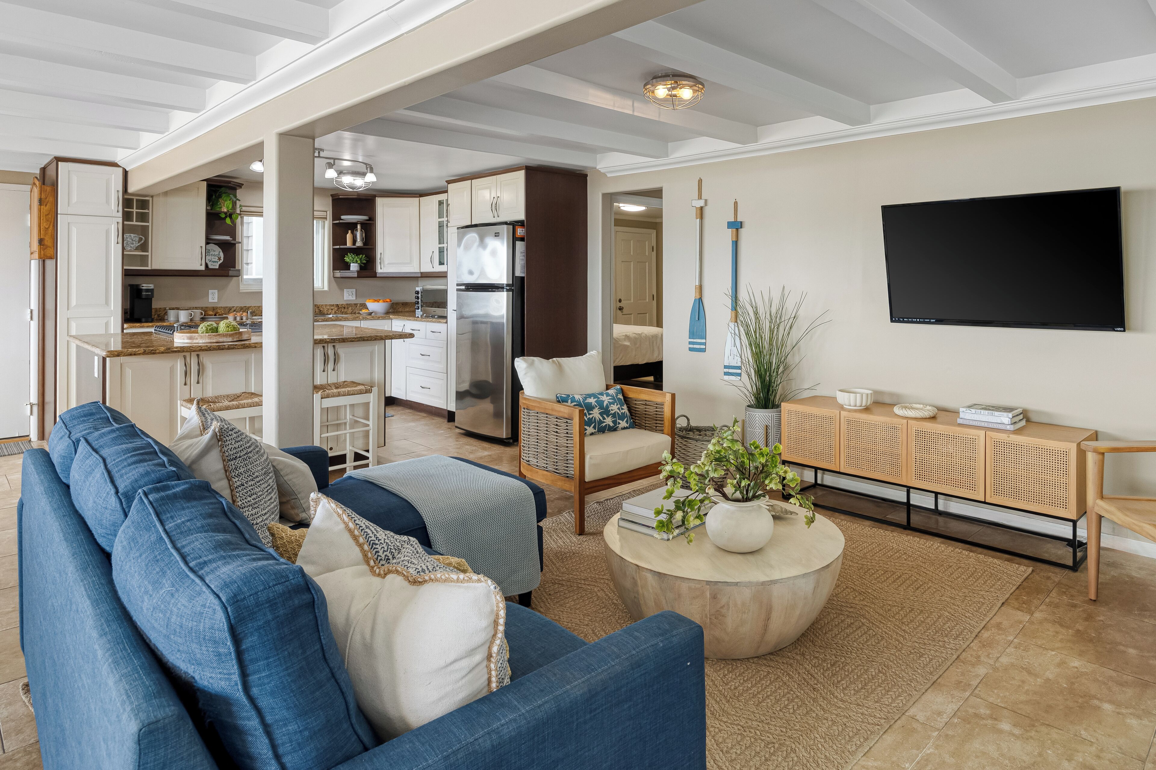 A spacious living room with a blue sofa, a wooden coffee table, and a TV mounted on the wall.