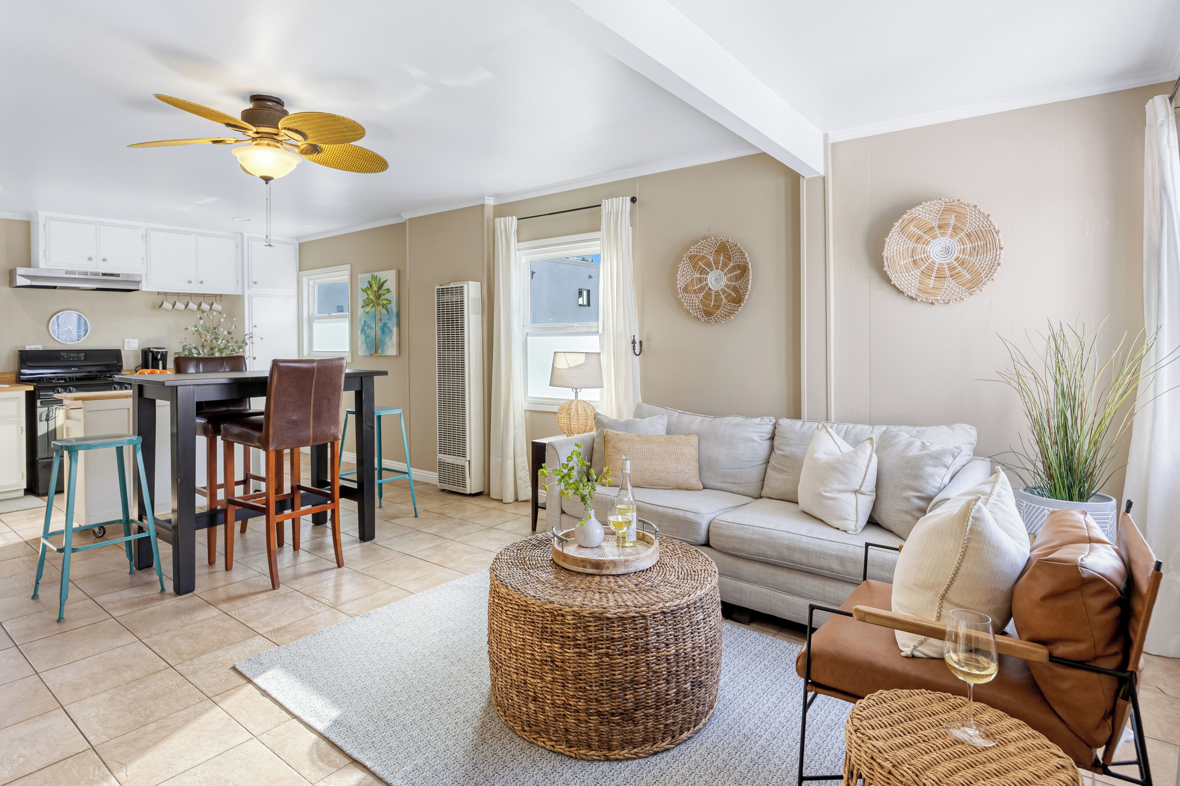 A modern living room with a sofa, coffee table, and chairs. There is a kitchen area with cabinets and a dining table.