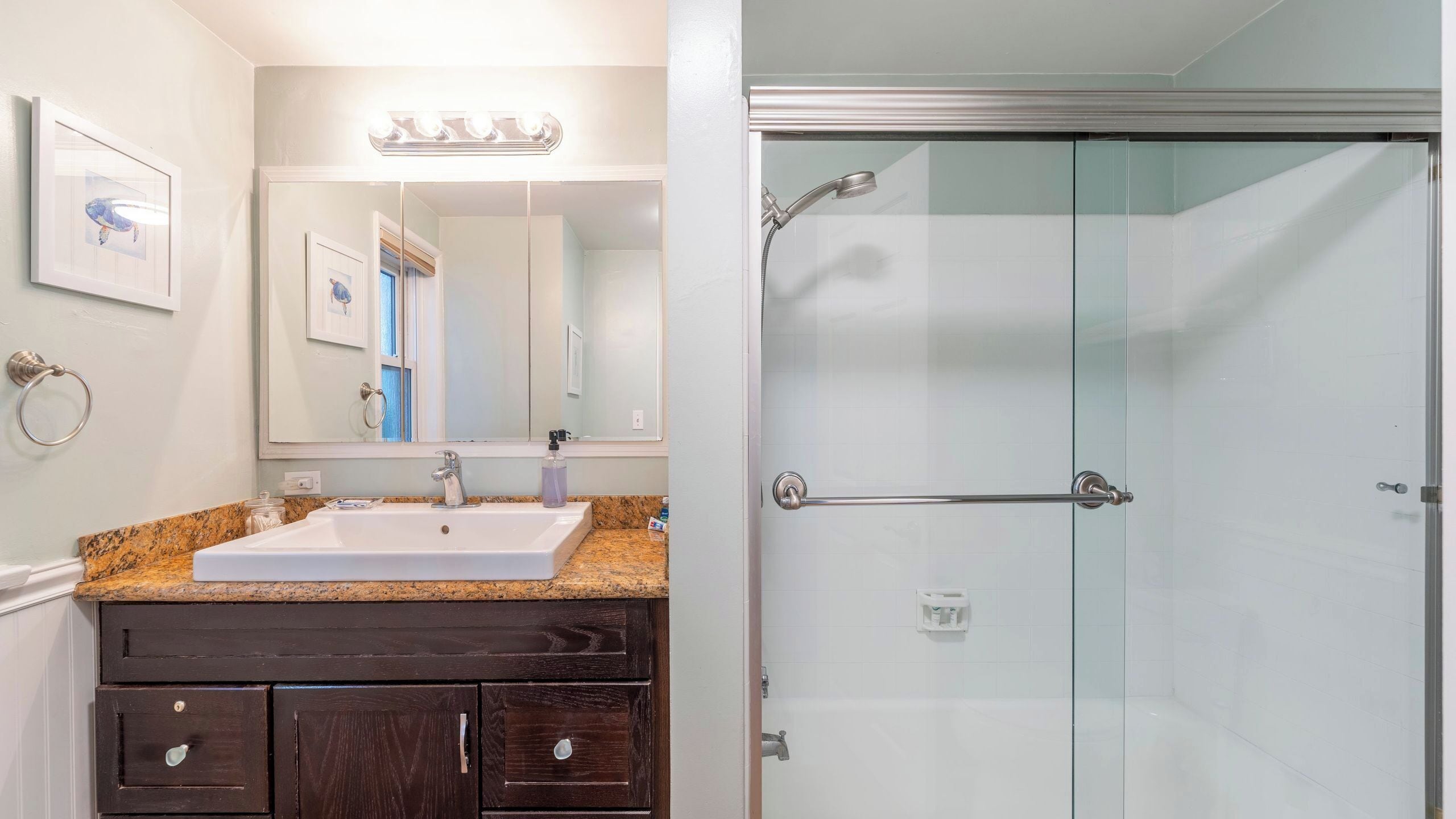 A bathroom with a sink, mirror, vanity, and a glass-enclosed shower.