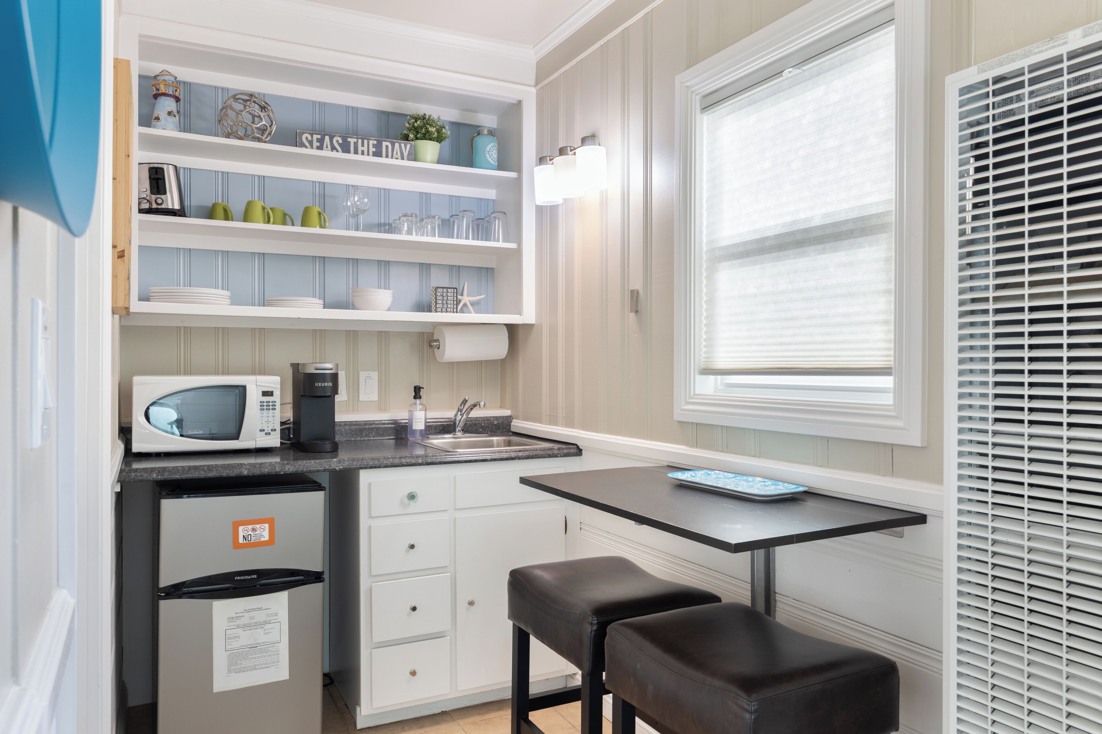 Una cocina compacta equipada con microondas, cafetera y una pequeña mesa de comedor con dos taburetes.