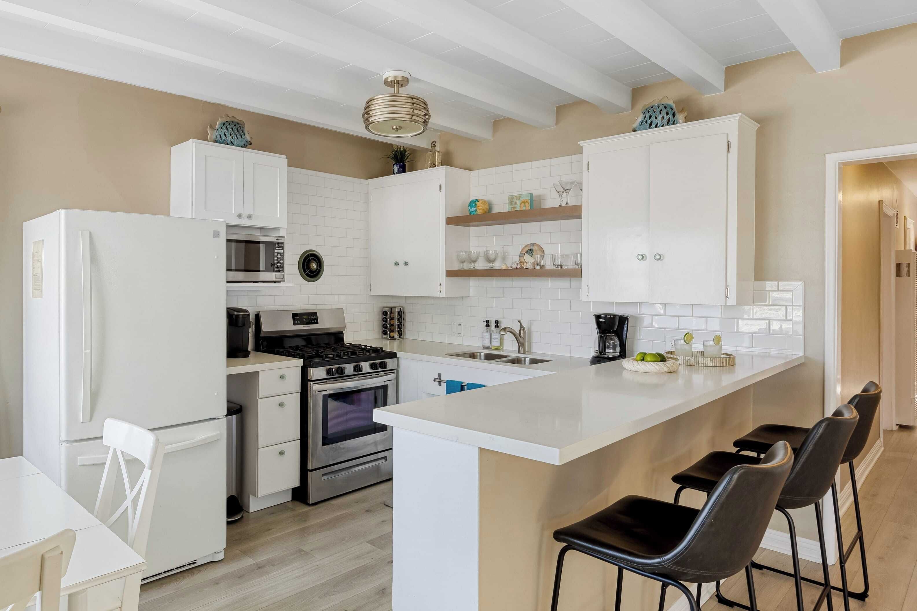 A modern kitchen with white cabinets, a central island, bar stools, a stove, oven, microwave, and a sink.