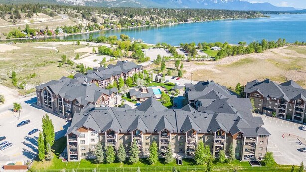 A resort with multiple buildings, a swimming pool, and a view of a lake and mountains.