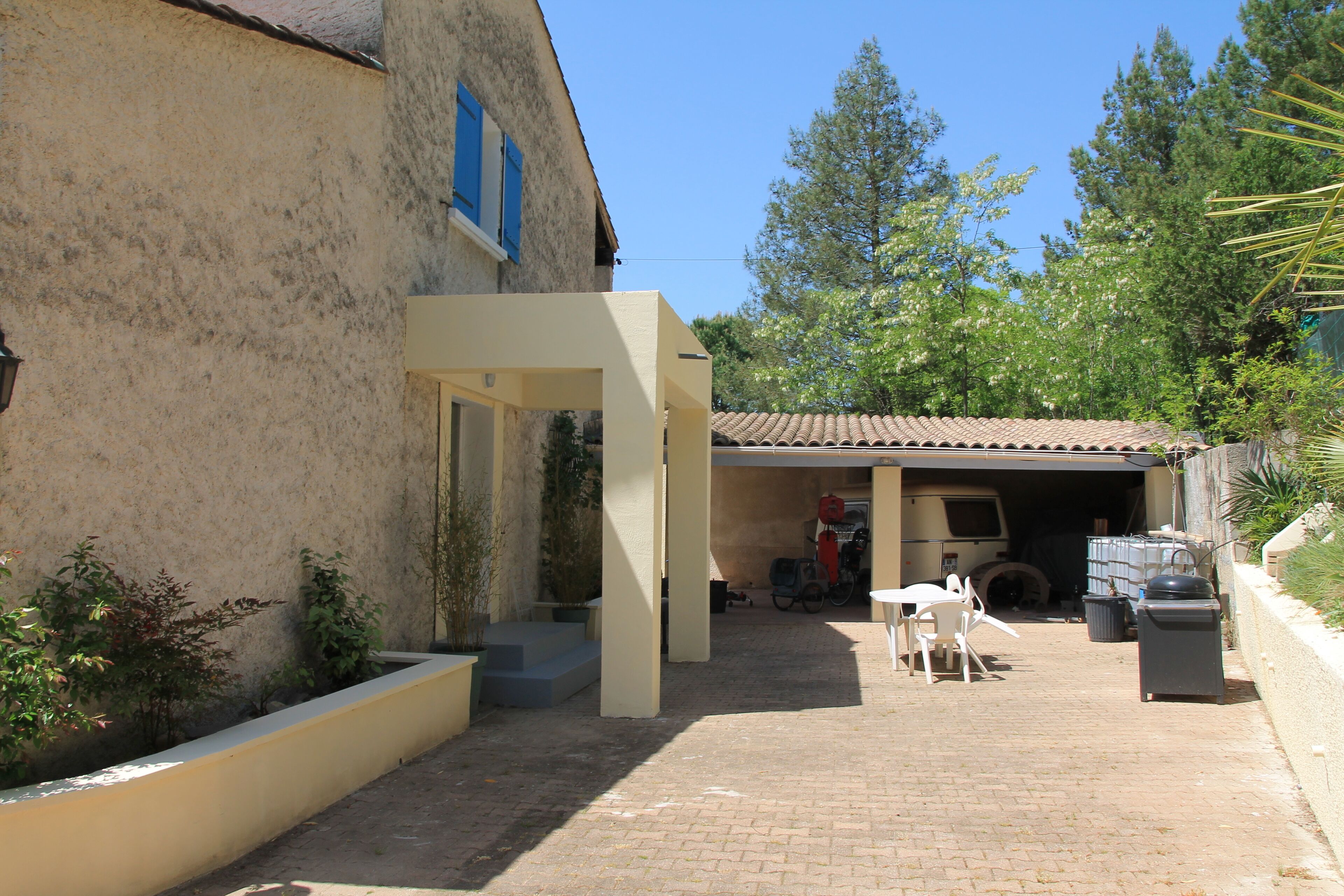 A courtyard with a covered seating area, a garage, and a vehicle.