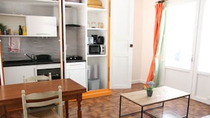 A compact kitchen with a dining area, a small table with a plant, and a window with curtains.