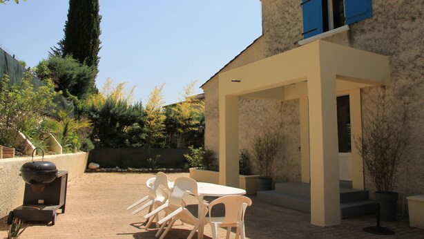 An outdoor patio with a table and chairs, a barbecue grill, and a stone wall.