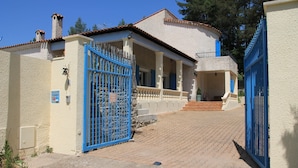 A building with a white exterior and blue gates, featuring a stone staircase leading to a covered area with a railing.