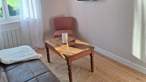 En stue med en brun lædersofa, et træbord, en rød stol, et fjernsyn monteret på væggen og et vindue med lette gardiner.
