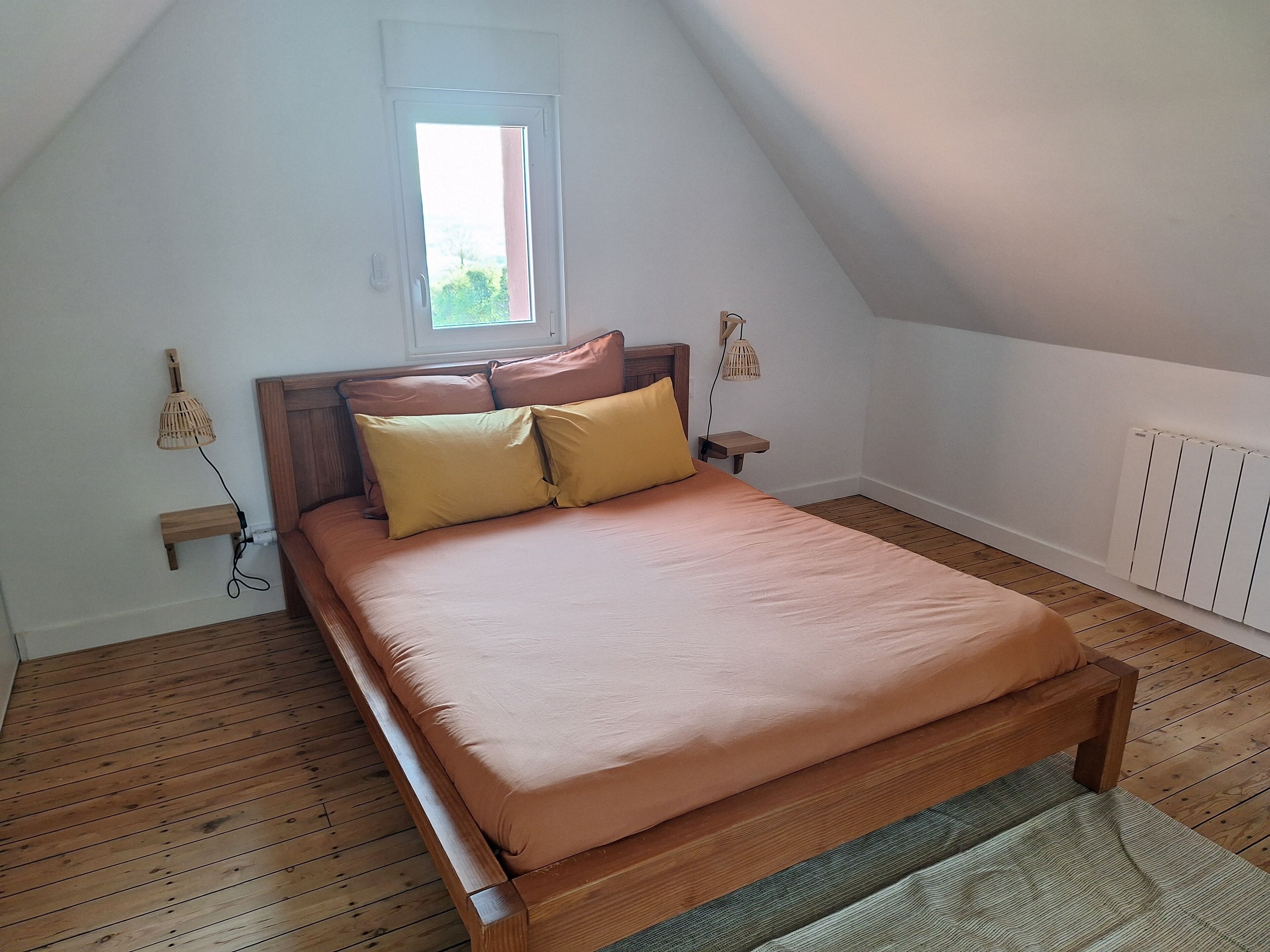 A single bed in a room with a sloped ceiling, a window, and a radiator.