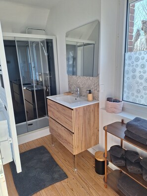 A modern bathroom with a glass shower enclosure, a wooden vanity with a mirror, and a window with a view of the outside.