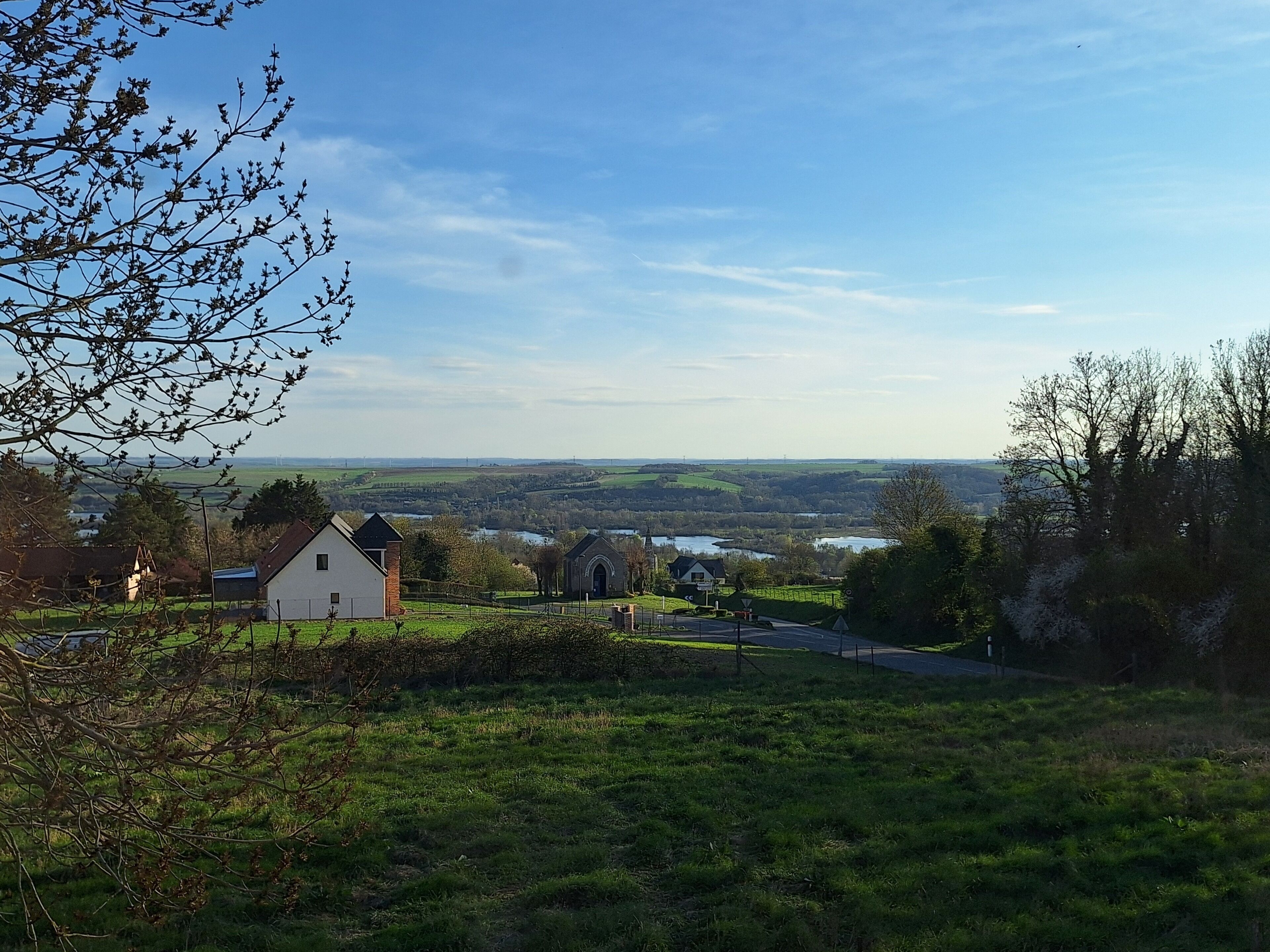 A rural landscape with a small white building, a church, and a road leading to a distant village.