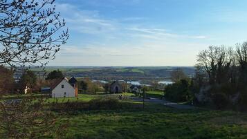 A rural landscape with a small white building, a church, and a road leading to a distant village.