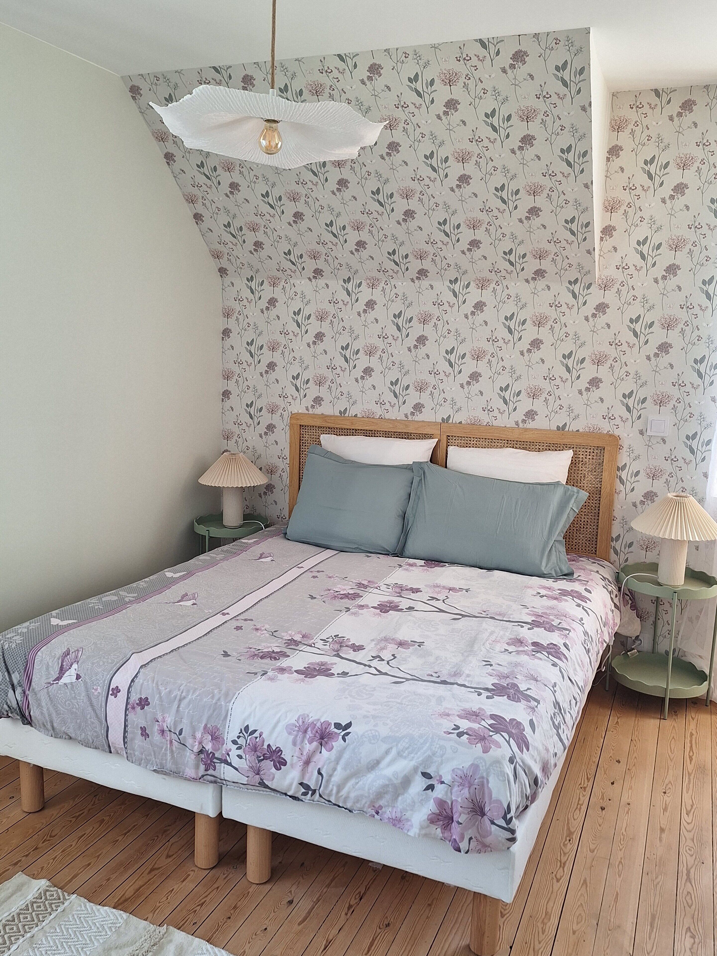 Un dormitorio con cubrecama estampado con motivos florales, cabecera de madera y dos lámparas de noche.