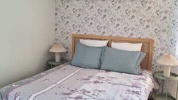 Un dormitorio con cubrecama estampado con motivos florales, cabecera de madera y dos lámparas de noche.