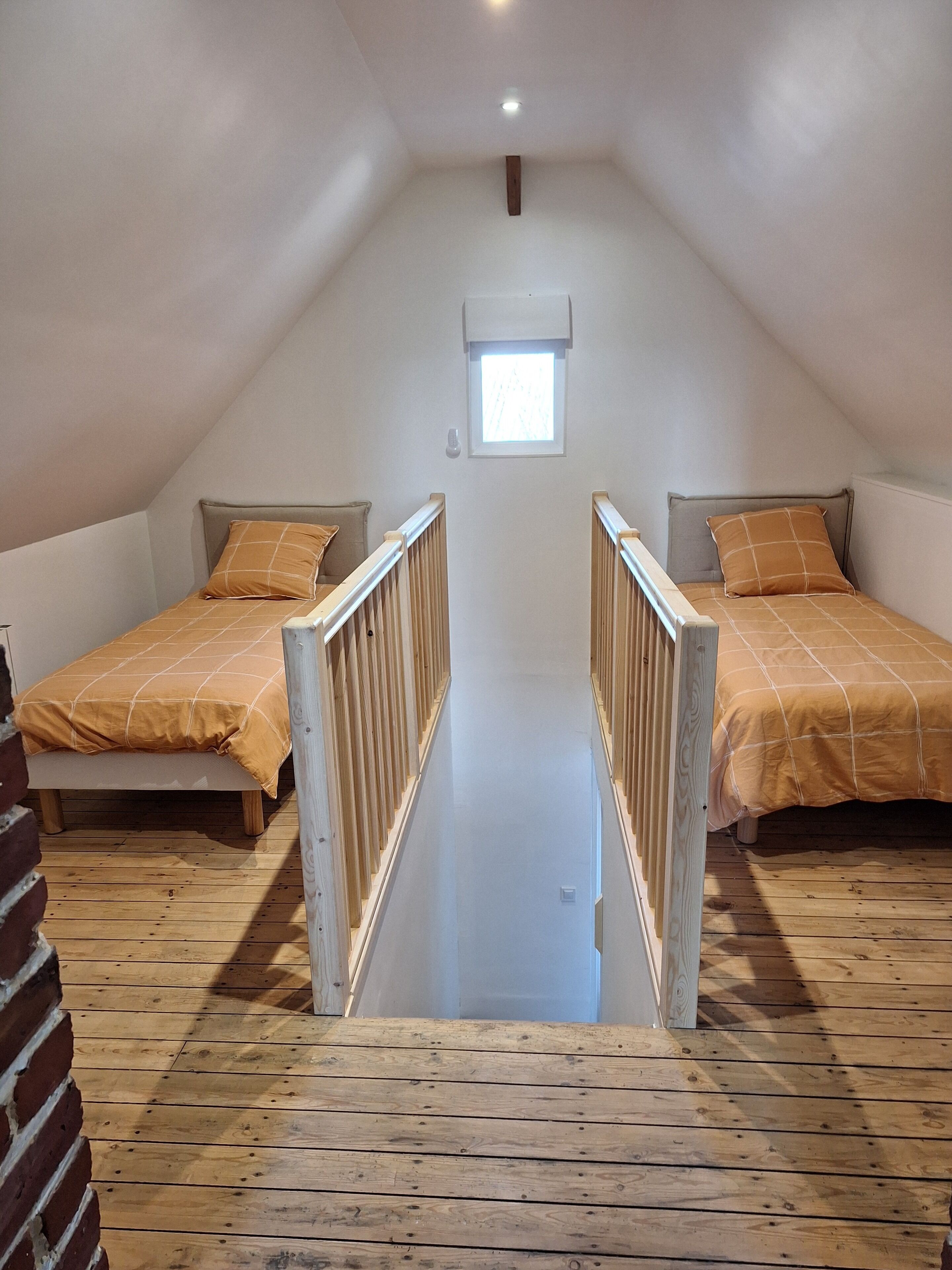 A high-ceilinged attic bedroom with two beds, wooden flooring, and a small window.