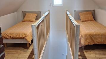 A high-ceilinged attic bedroom with two beds, wooden flooring, and a small window.