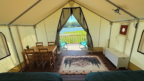 Een tentaccomodatie met twee bedden, een eethoek en uitzicht op een meer.