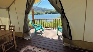 Een tent met uitzicht op een meer, een houten tafel, twee stoelen en een vloerkleed met dierenprint.