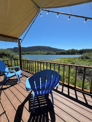 A wooden deck with blue chairs, a canopy, and a view of a lake and forest.