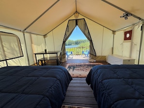 A tent with two beds, a table, and a view of the outdoors.