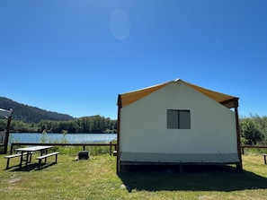 A small, single-story cabin with a pitched roof, a window, and a door, situated on a grassy area with a picnic table nearby.