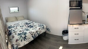 Une petite chambre comprenant un lit, une kitchenette et une petite fenêtre.