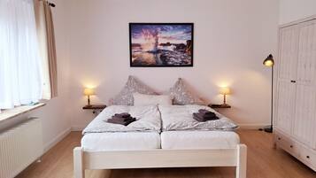Ein Schlafzimmer mit einem weißen Bett, gemusterten Kissen, einem gerahmten Bild an der Wand und einer Heizung.
